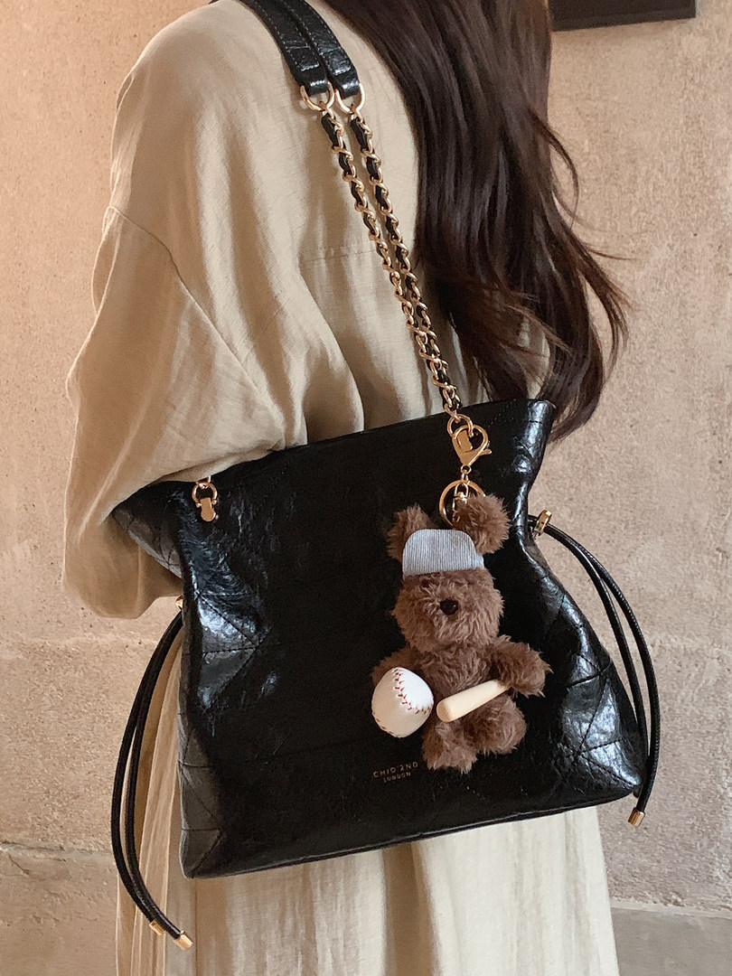 Black leather handbag with chain strap and teddy bear charm worn on a model