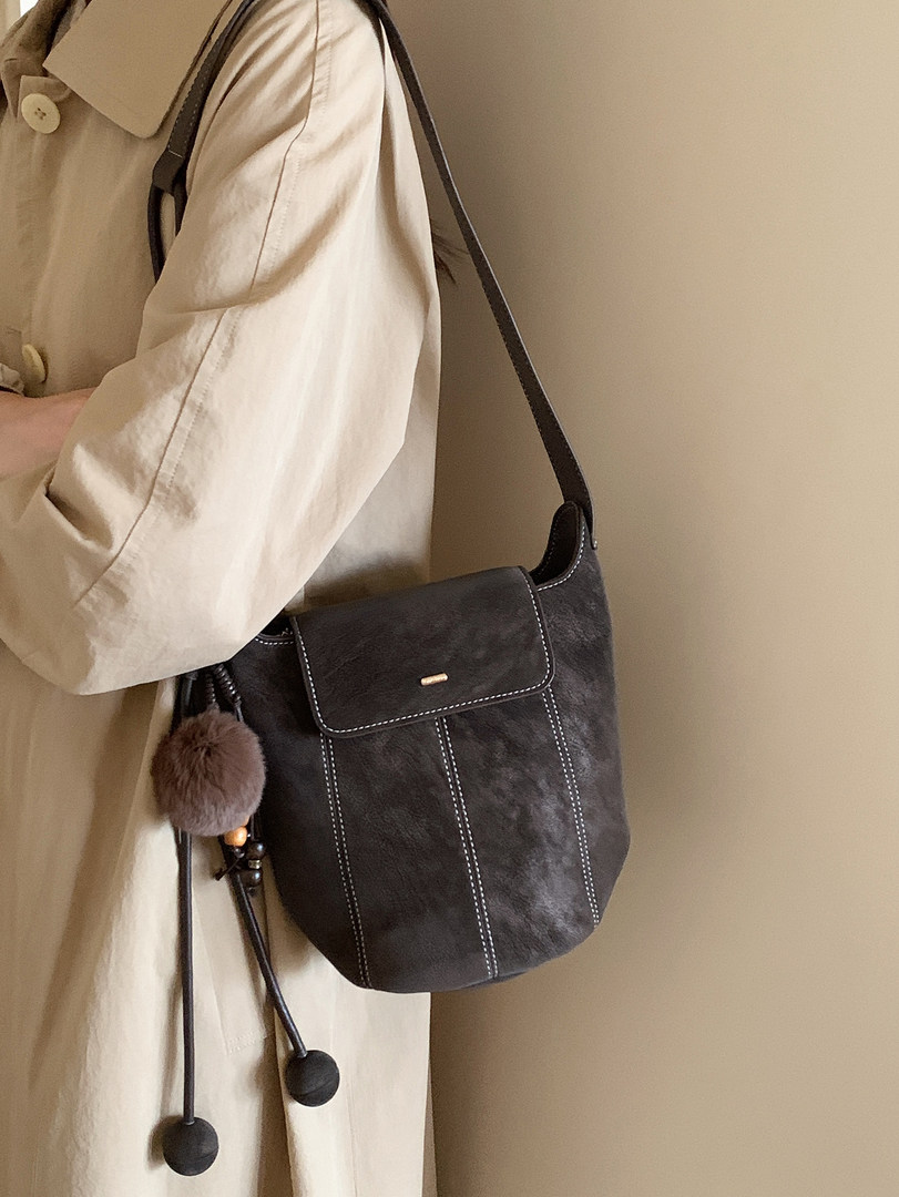 Black shoulder bag worn crossbody over a beige trench coat