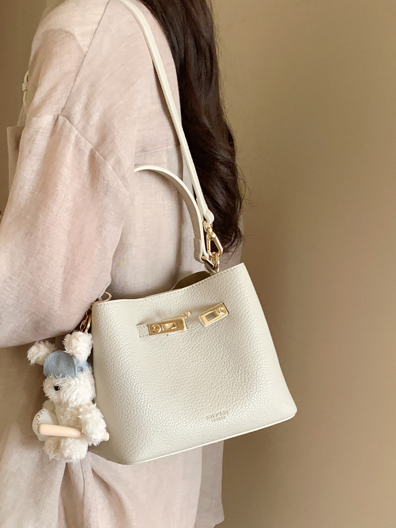 White leather shoulder bag with gold hardware and a charm, worn on a model