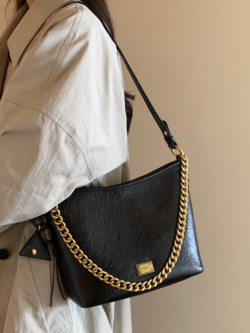 Black shoulder bag with gold chain strap worn on a model
