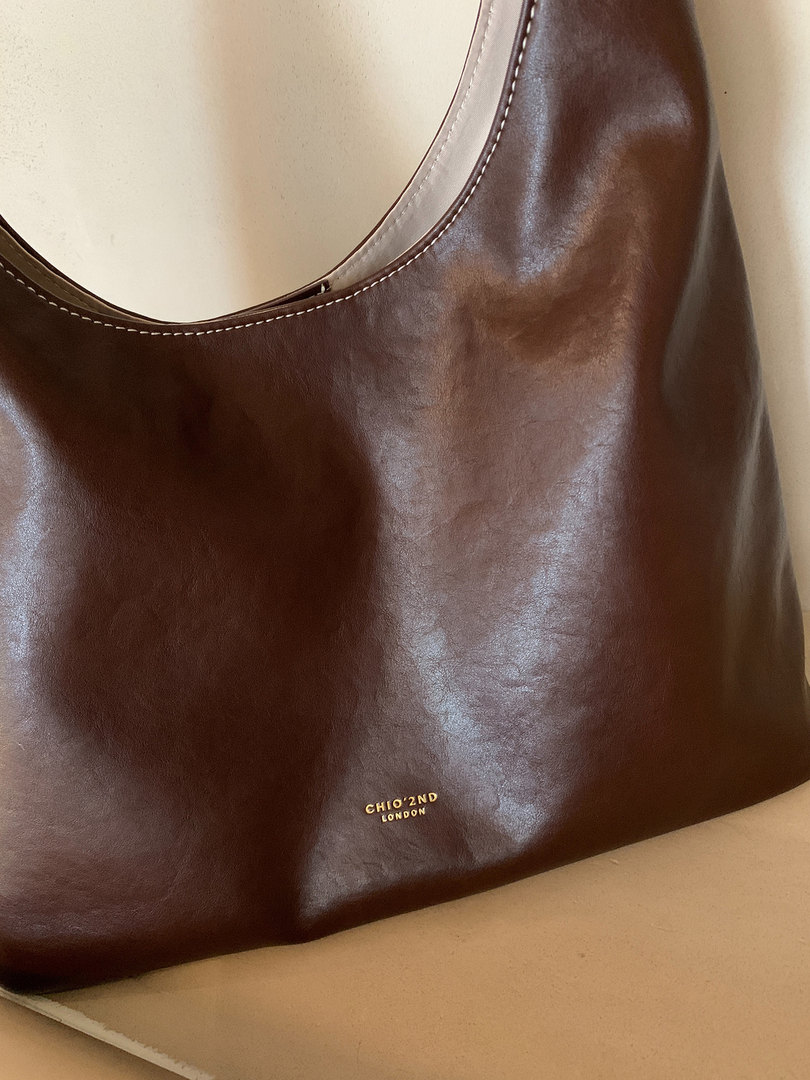 Brown leather handbag with gold logo on a neutral background