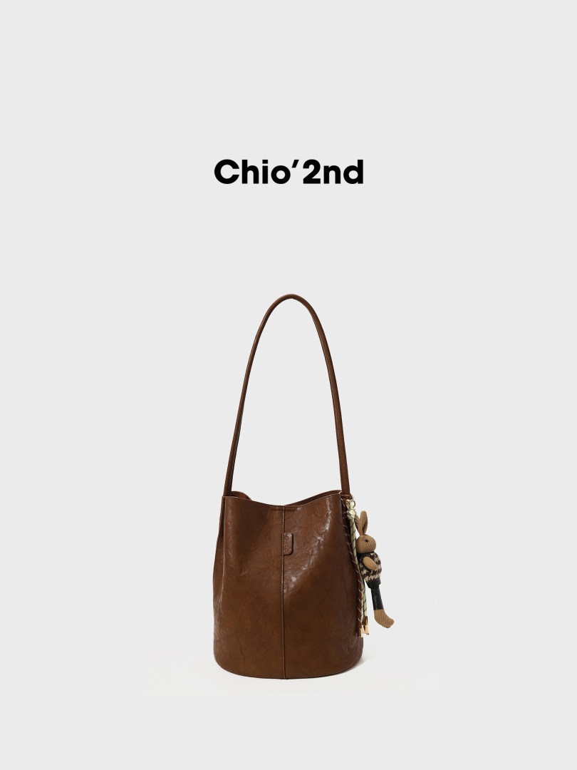 Brown leather shoulder bag with long strap and hanging charm on white background