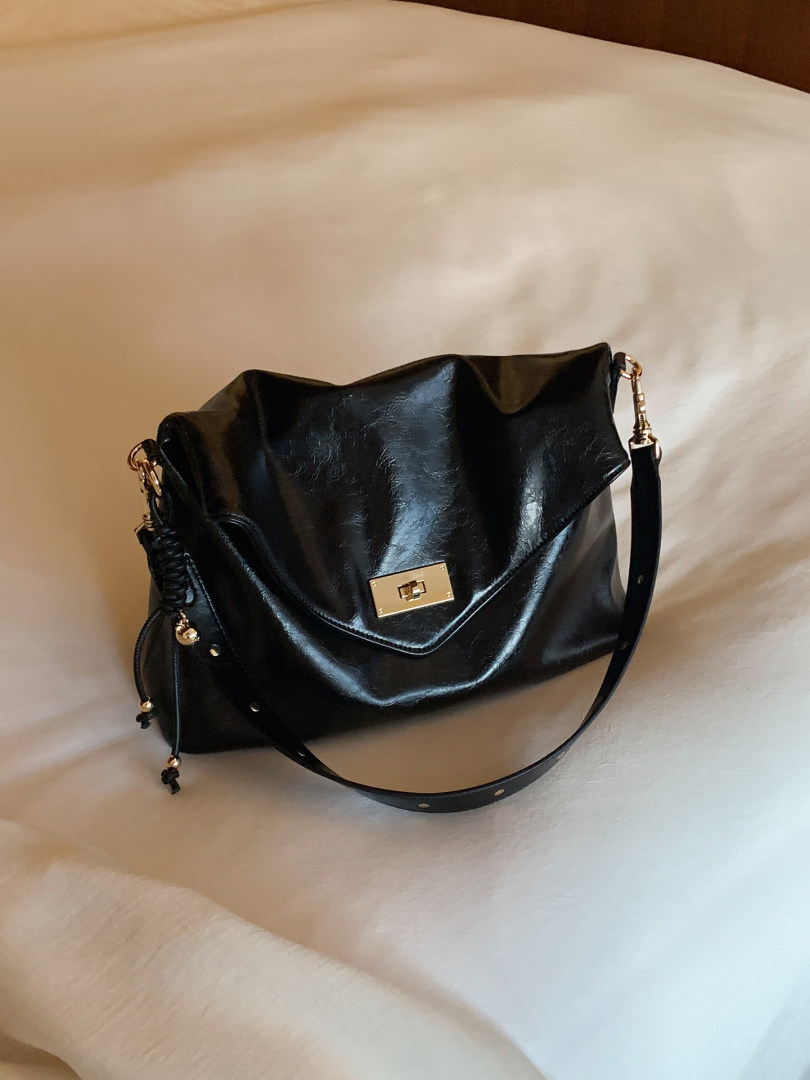 Black leather shoulder handbag with gold hardware on a bed