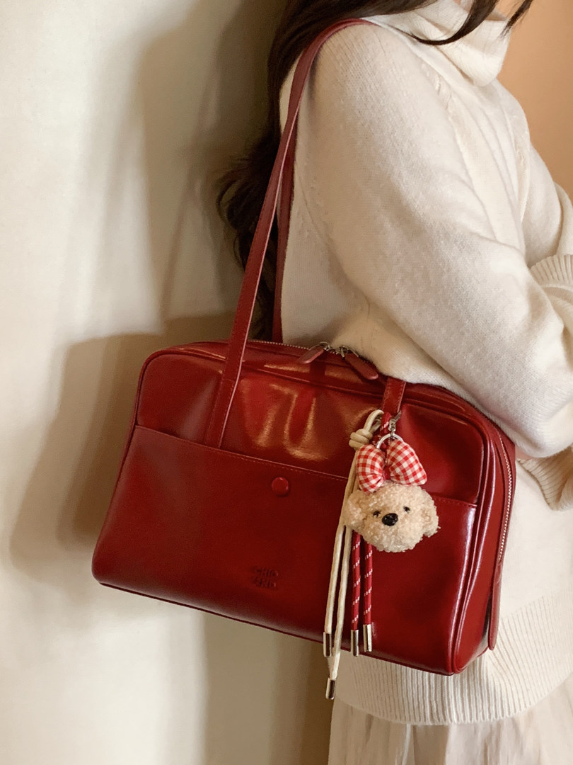 Red leather shoulder handbag worn by a person with a small teddy keychain