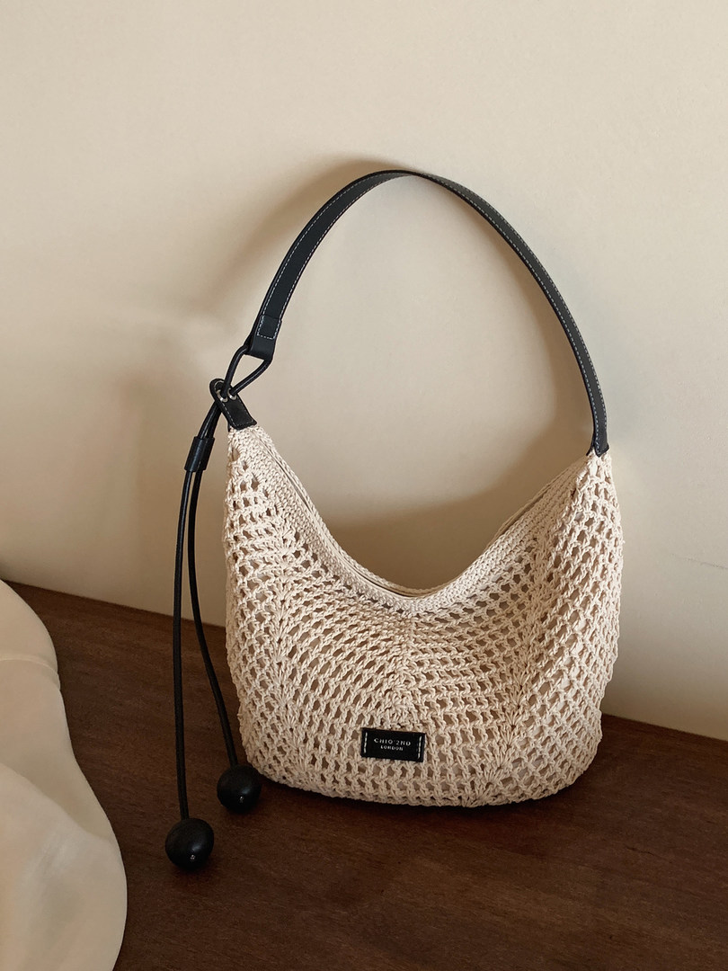 Beige woven crochet shoulder bag with black strap on a tabletop