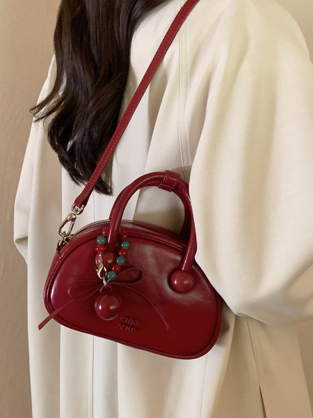 Red leather handbag worn crossbody on a cream outfit