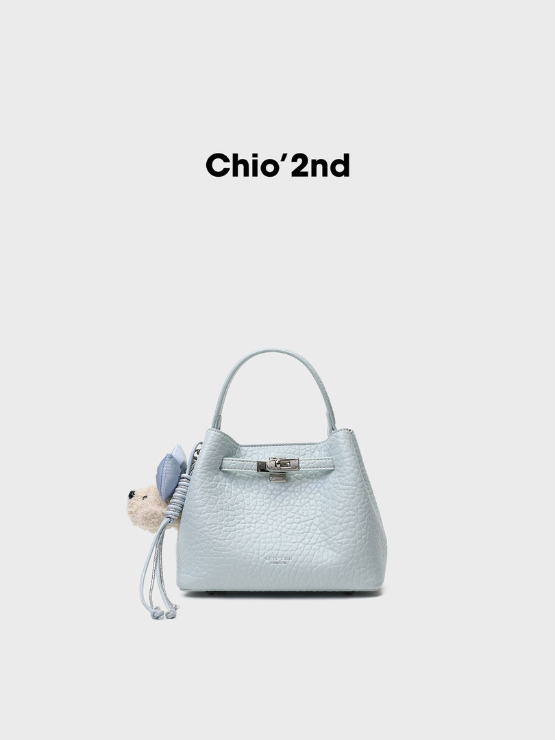 Light blue textured handbag with a small charm on a white background