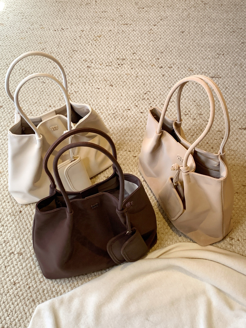 Assorted neutral tote handbags displayed on a carpet