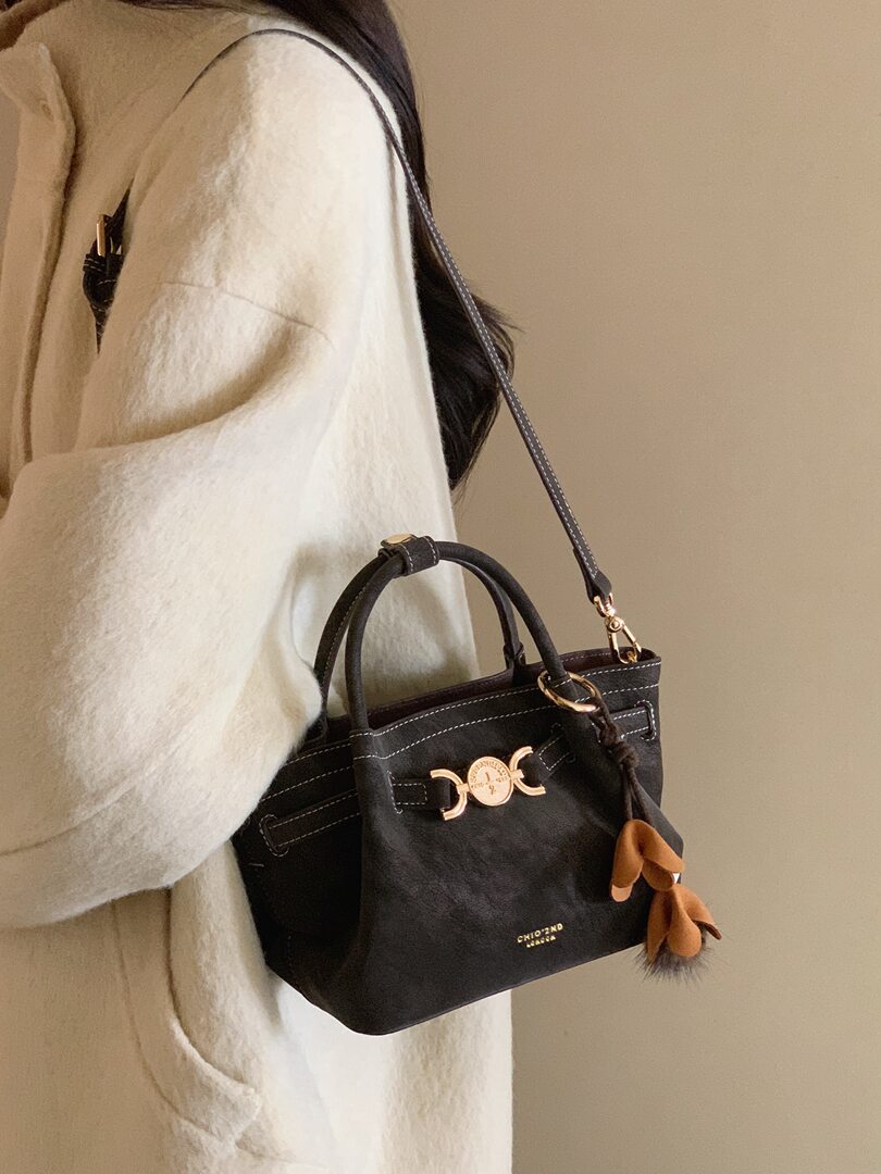 Black structured handbag worn on a model with a shoulder strap and gold hardware