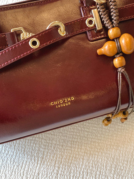 Close-up of a burgundy leather handbag with gold hardware and bead tassel detail