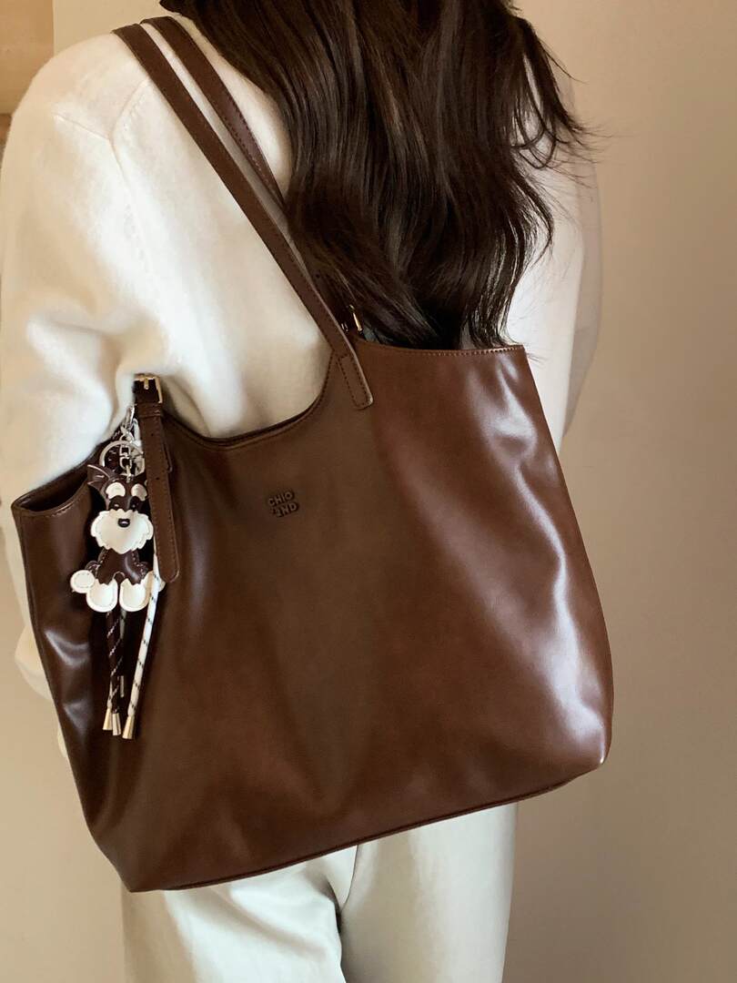 Brown leather tote bag worn over a cream outfit