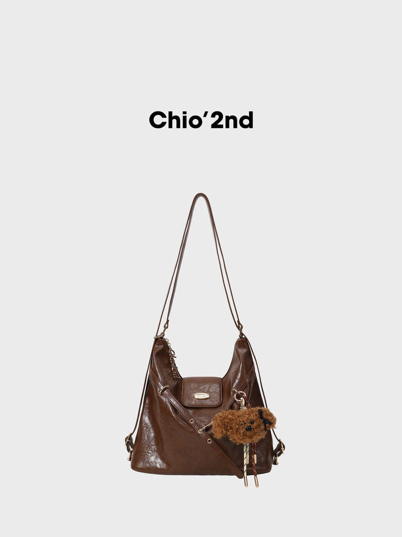Brown leather shoulder bag with a plush teddy charm on a white background