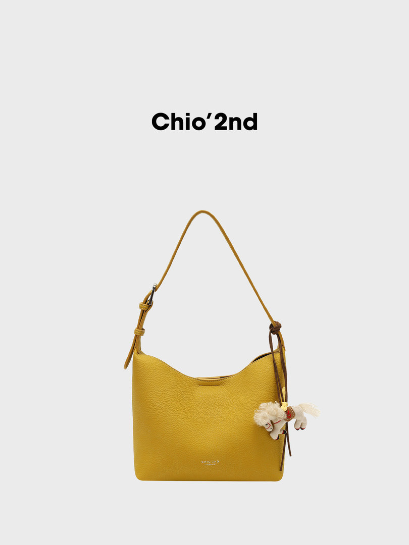 Yellow leather shoulder bag with a long strap and charm on a white background