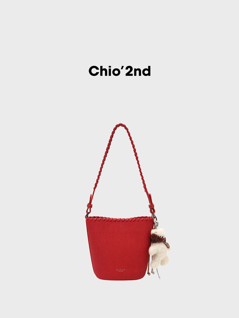 Red handbag with braided strap and teddy bear charm on a white background