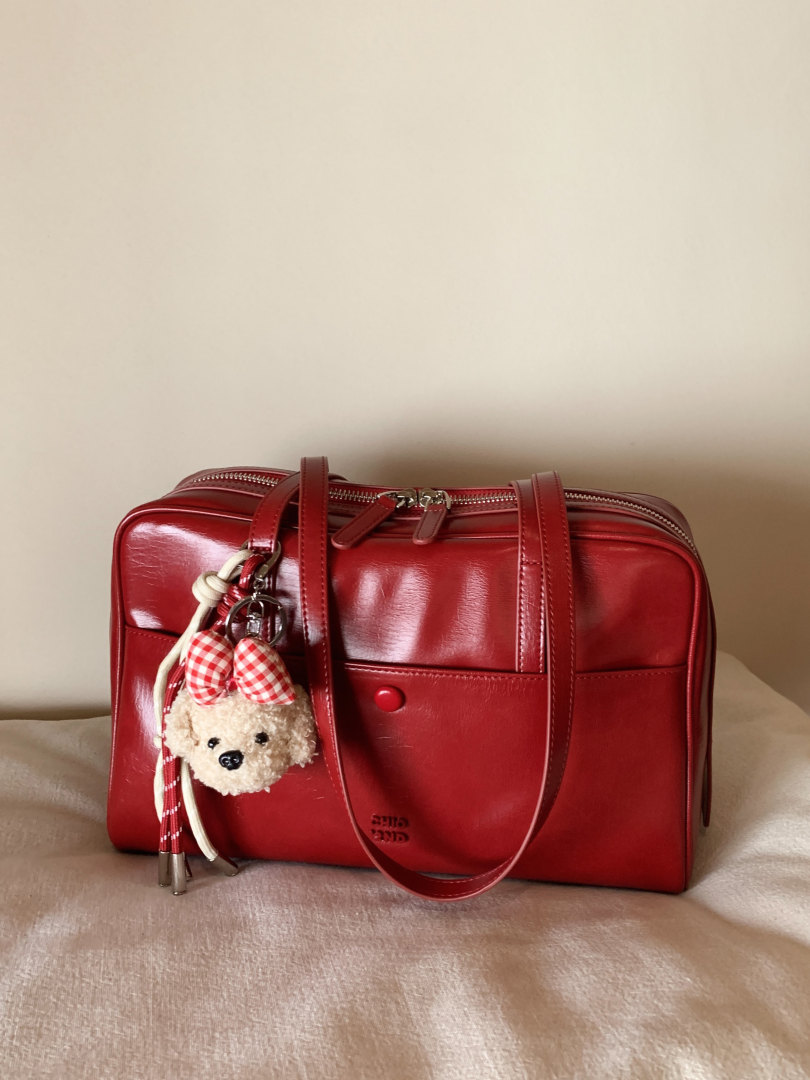 Red glossy leather handbag with shoulder straps and teddy bear keychain