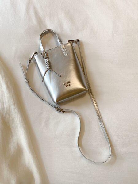 Silver mini handbag with long shoulder strap on fabric background