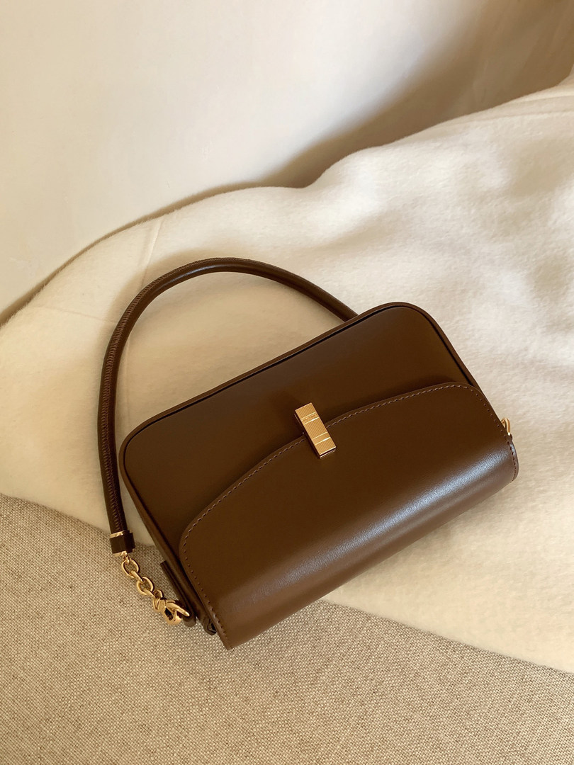 Brown leather shoulder handbag with gold hardware on a neutral fabric background