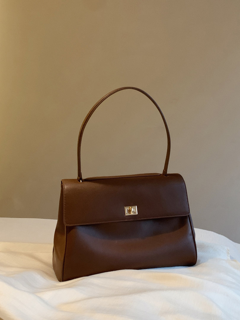 Brown leather handbag with top handle on a bed