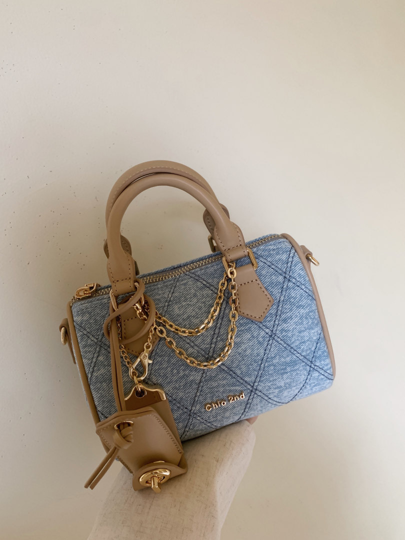 Blue denim handbag with tan leather handles and gold chain details