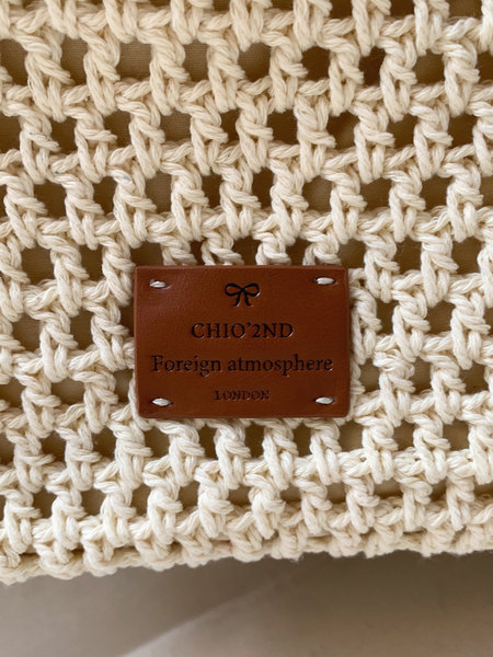 Close-up of a cream woven crochet bag with a brown leather brand label