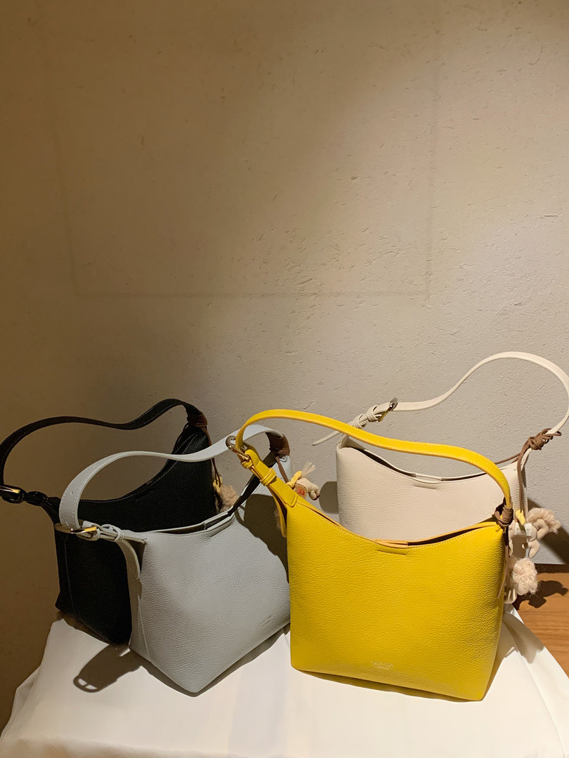Three small leather shoulder bags in black, light gray, and yellow on a table