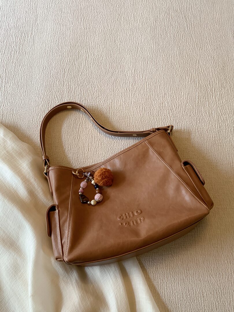 Brown leather shoulder handbag with decorative charm on a textured bedspread