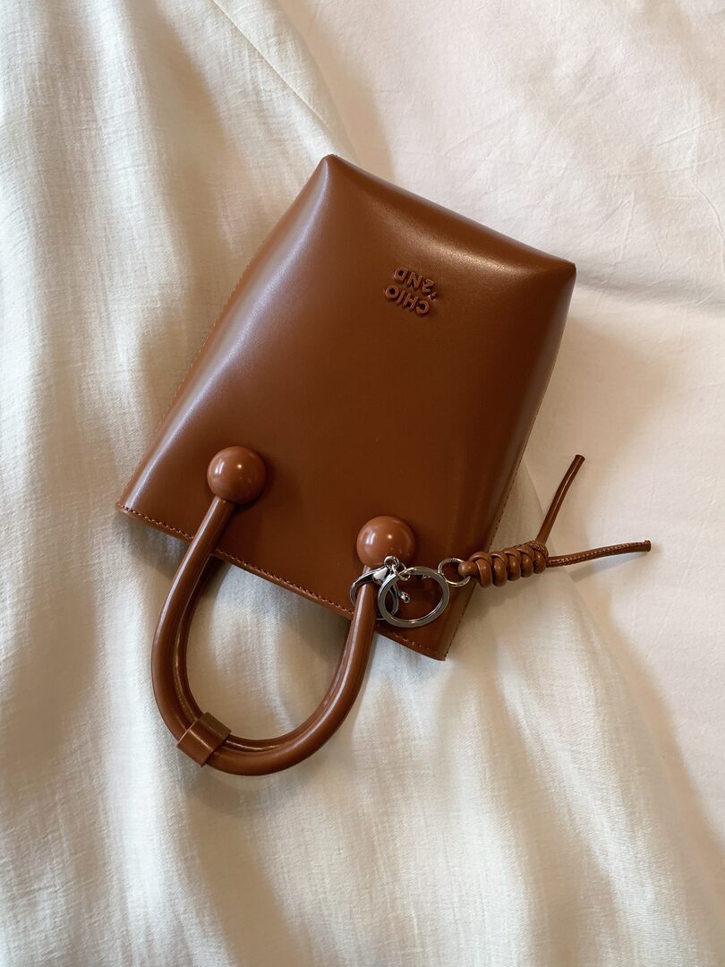 Brown leather handbag with top handles and keychain on a light fabric background