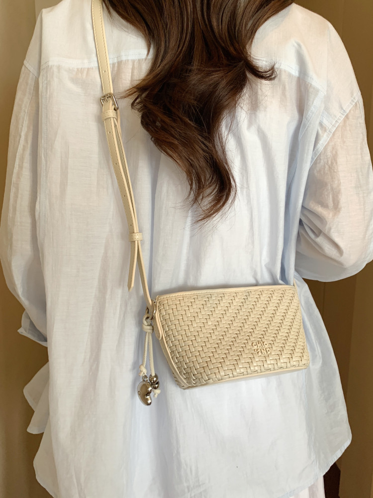 Cream woven crossbody bag worn on a model