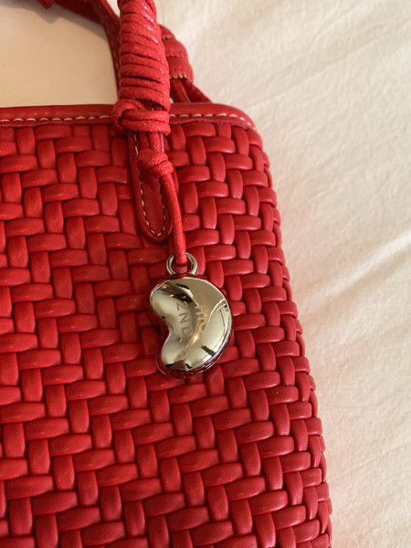 Red woven handbag with a metallic charm on a white background
