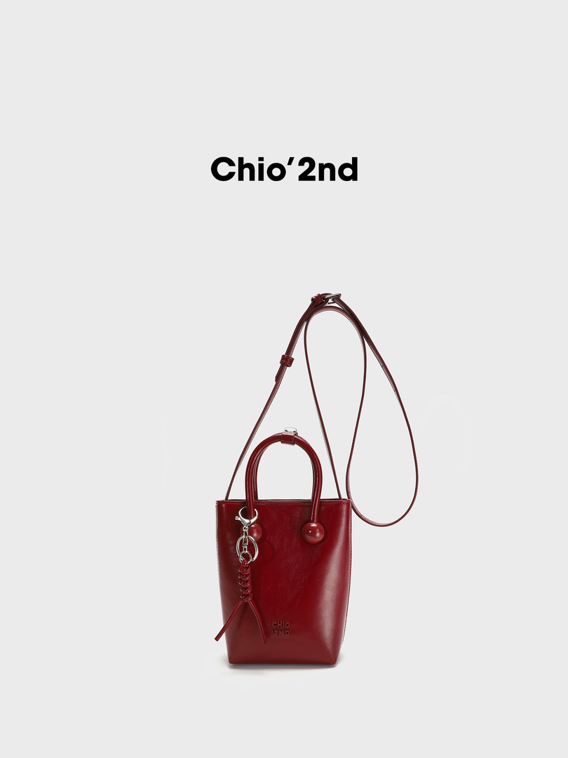 Red leather bucket handbag with long shoulder strap on a white background