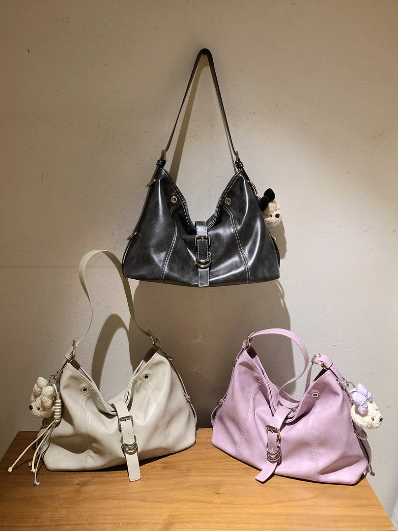 Three hobo-style shoulder bags in black, beige, and pink on display