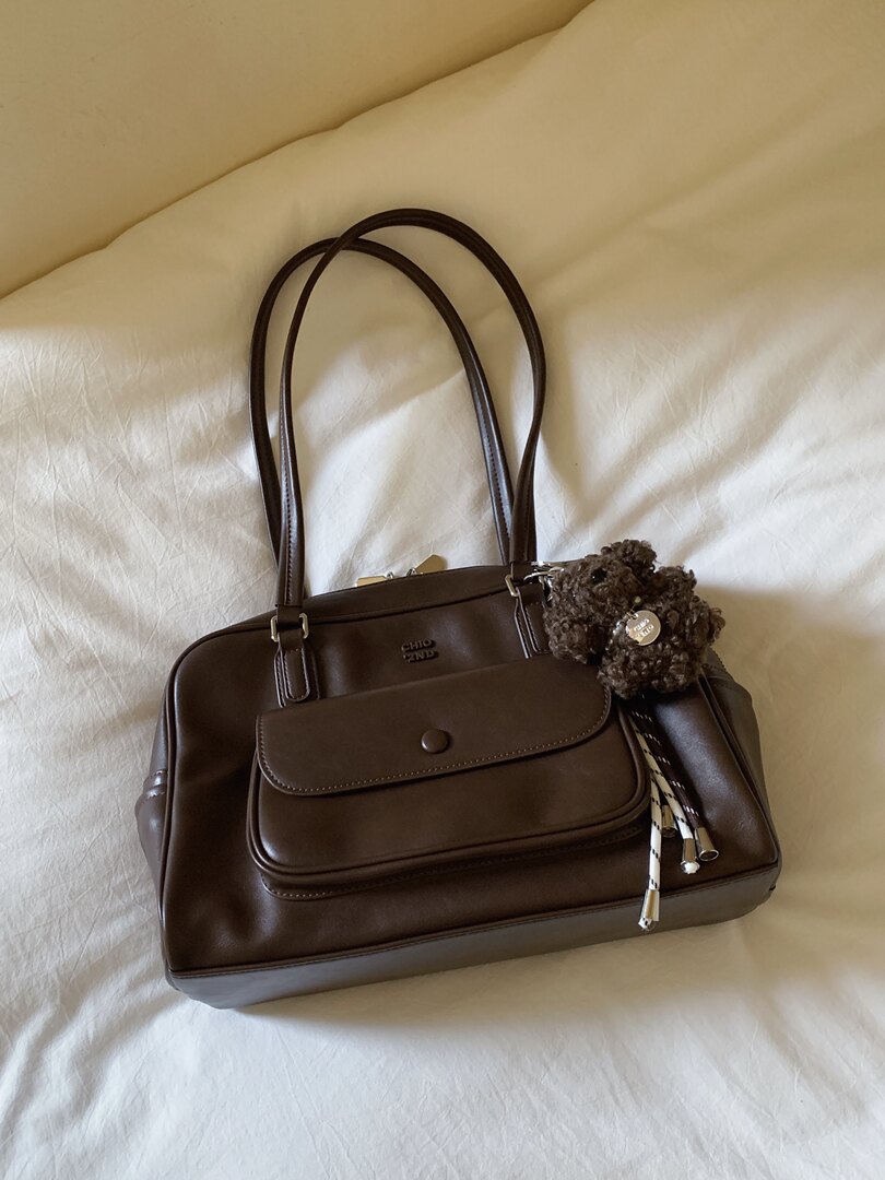 Brown leather handbag with long handles and a front flap pocket on a bed
