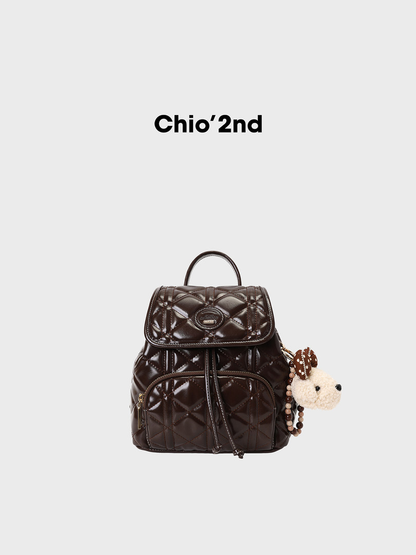 Dark brown quilted backpack with a small plush charm on a white background