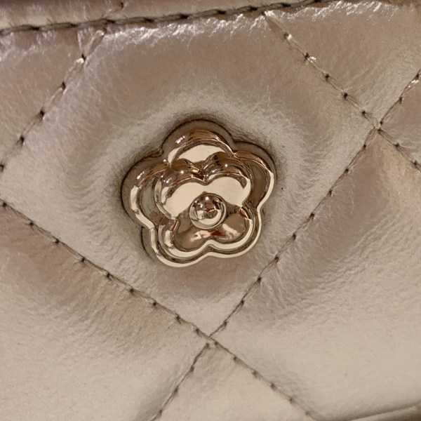 Close-up of a quilted beige leather bag with a gold flower-shaped clasp