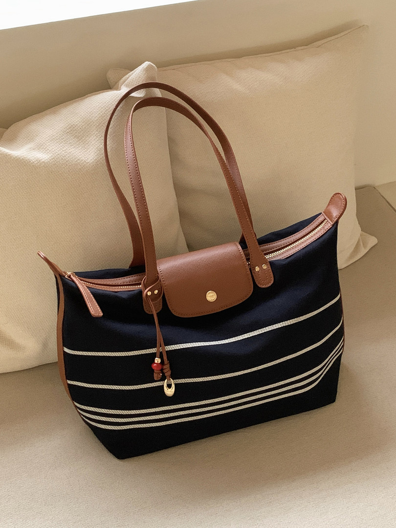 Navy and brown tote handbag with long handles on a beige sofa