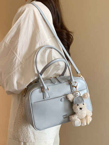 Light blue handbag worn over the shoulder with a teddy bear keychain charm