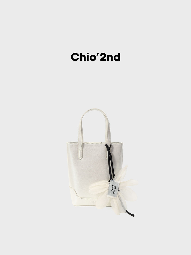 White mini tote handbag with flower charm on a plain background