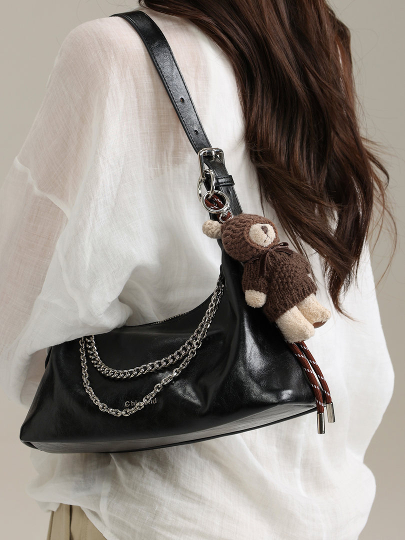 Black leather shoulder bag worn by a model with a chain detail and teddy charm