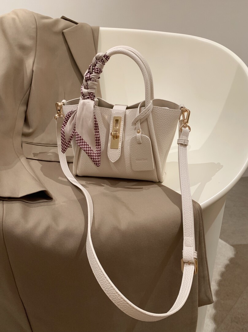 Cream leather handbag with scarf detail and gold hardware on a chair