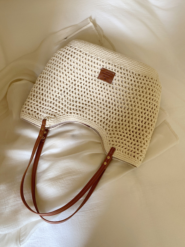 Cream crochet woven tote bag with brown leather handles on a light fabric background