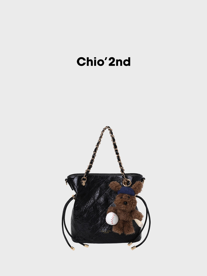 Black leather handbag with chain strap and teddy bear charm on white background