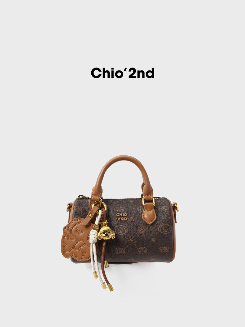 Brown mini handbag with leather handles and decorative charms on a white background