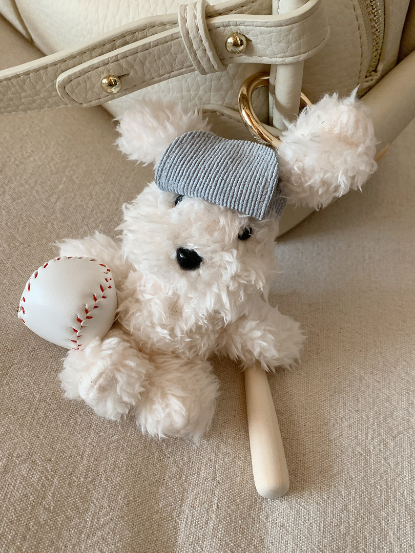 Fluffy teddy bear bag charm attached to a cream handbag