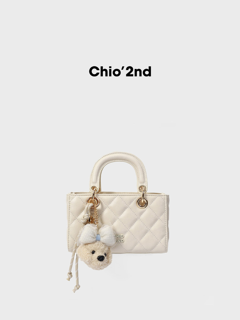 Cream quilted mini handbag with teddy bear charm on white background