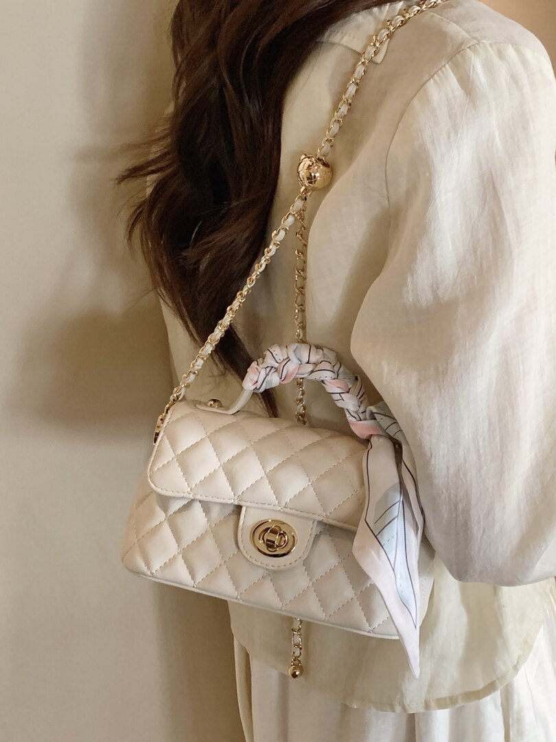 Cream quilted chain shoulder bag with gold hardware worn on a model