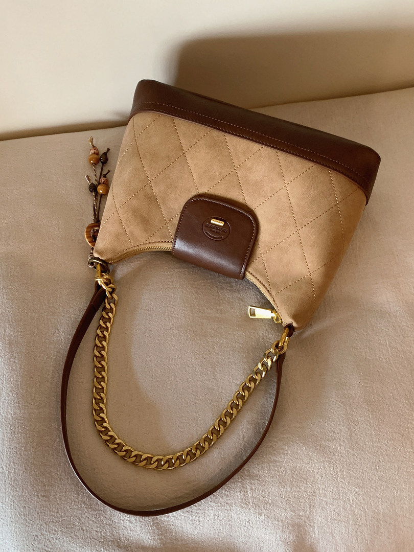 Beige quilted handbag with brown trim and gold chain strap on a neutral background