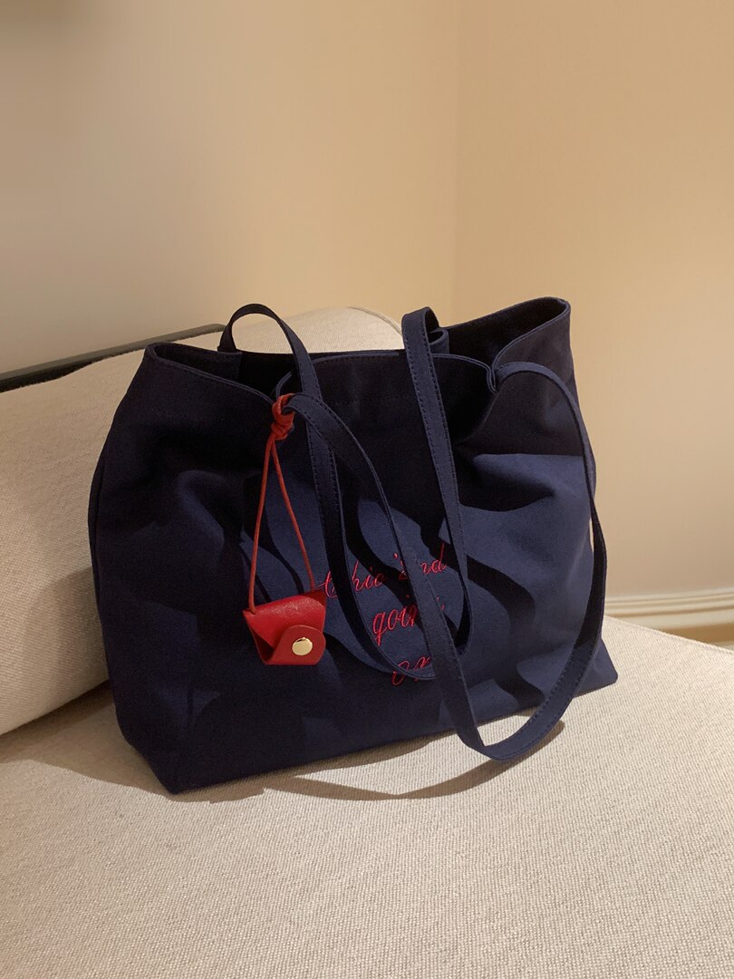 Navy tote bag with long straps and a red charm on a chair