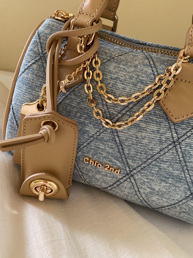 Close-up of a blue denim and tan leather handbag with gold chain hardware