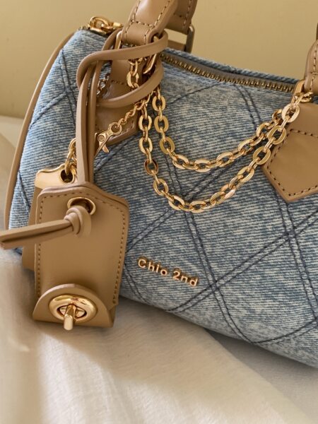 Close-up of a blue denim and tan leather handbag with gold chain hardware