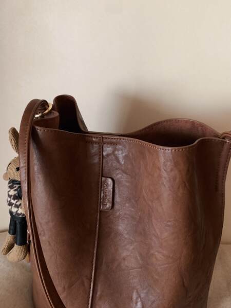 Brown leather tote bag with a woven charm hanging on the side